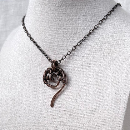 A dark copper wire-wrapped spiral pendant necklace displayed on a white fabric jewellery bust.