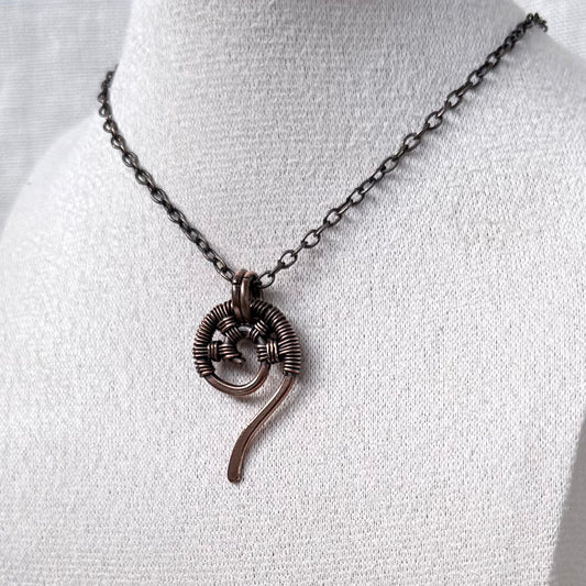 A dark copper wire-wrapped spiral pendant necklace displayed on a white fabric jewellery bust.