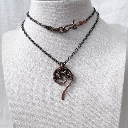 A copper necklace spiral pendant and copper chain, displayed on a white fabric mannequin bust. 