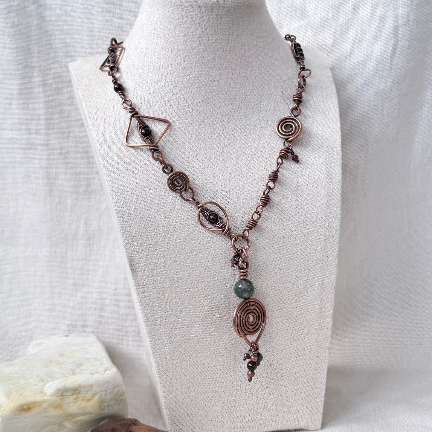 A bohemian-style copper wire necklace with spiral, geometric, and bead details, displayed on a white fabric mannequin bust.
