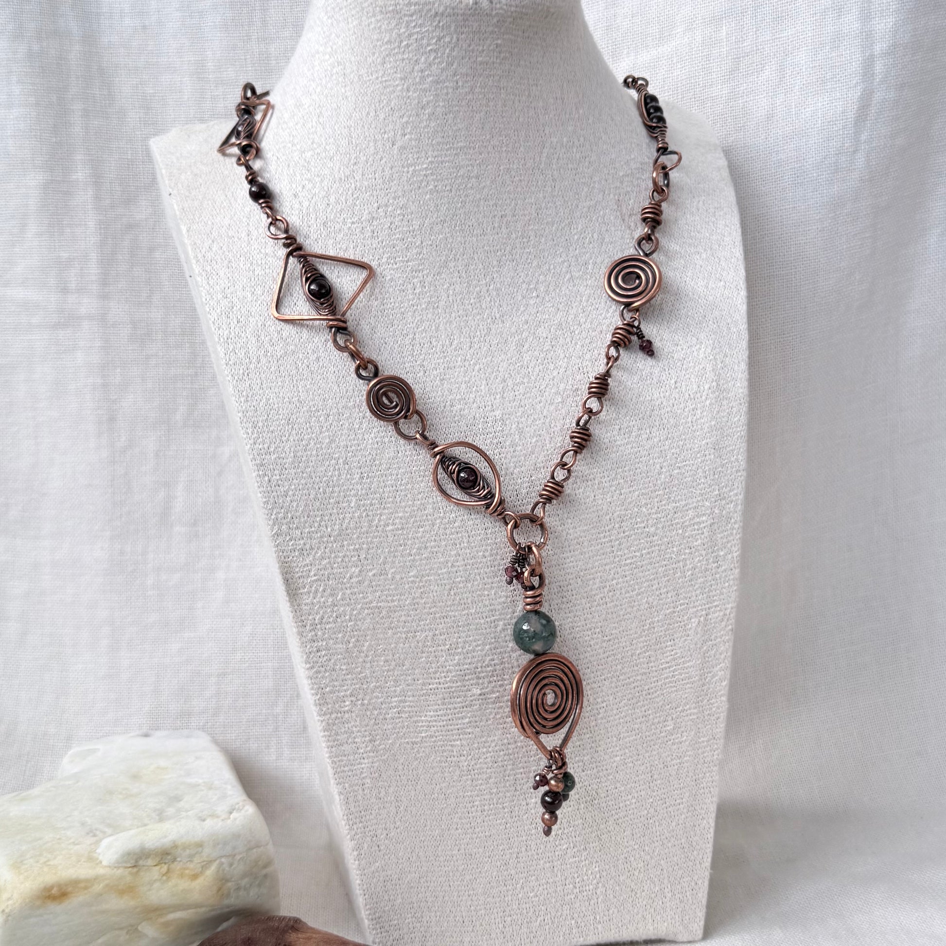 A bohemian-style copper wire necklace with spiral, geometric, and bead details, displayed on a white fabric mannequin bust.