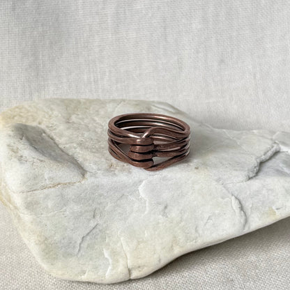 A multi-strand copper wire ring with a twisted center, displayed on a light-colored stone against a neutral linen background.