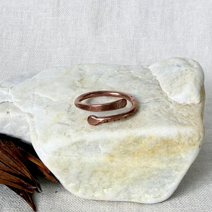 A hammered copper open wrap ring displayed on a light-colored stone slab against a neutral linen background.
