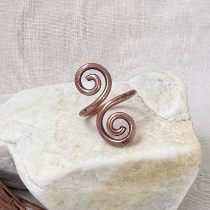 A copper spiral wrap ring displayed on a light-colored stone against a neutral fabric background.