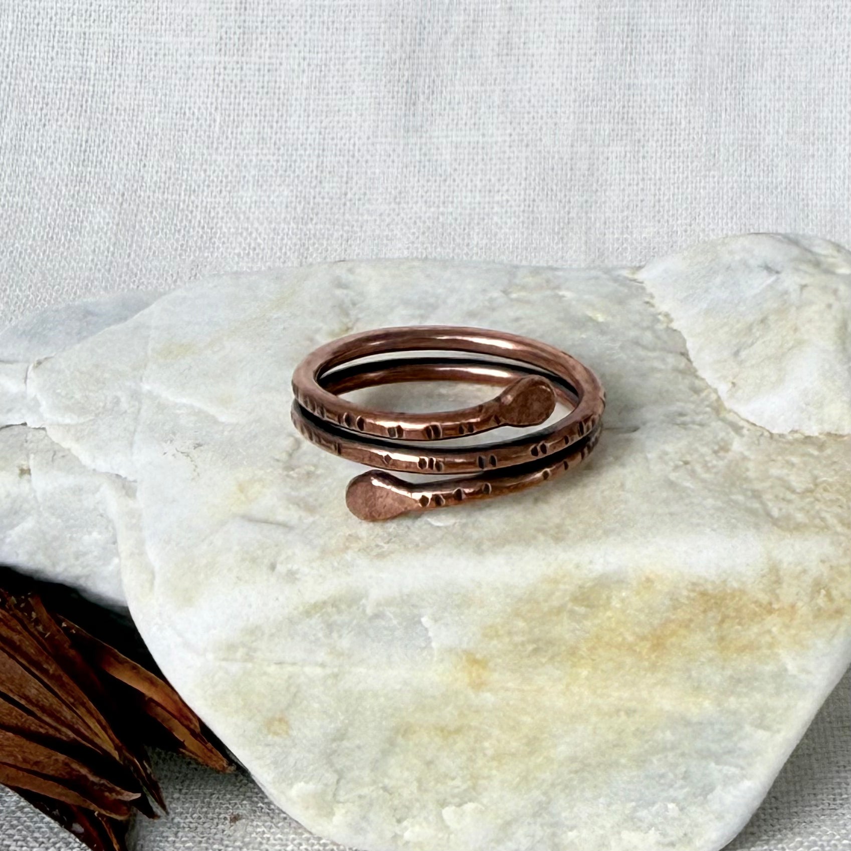 A handmade copper open wrap ring with hammered texture details, displayed on a light-colored stone surface.