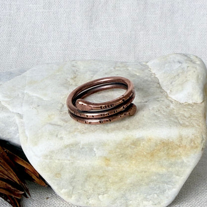 A wire copper ring displayed on a light-colored stone against a neutral linen background.